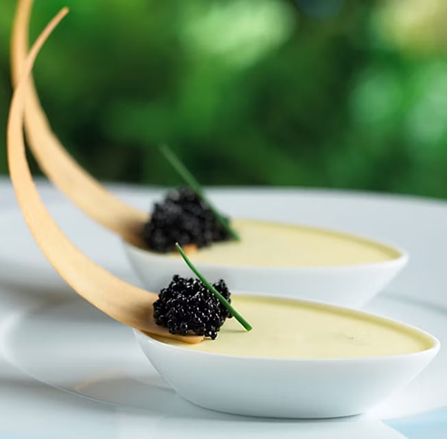 An elegant custard desert topped with a blackberry, served in a spoon